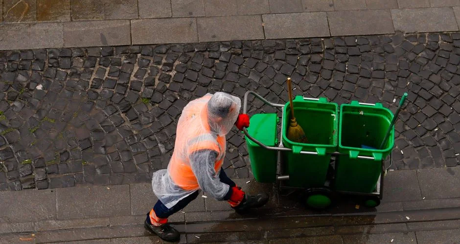 Close-up of hand cleaning window with squeegee outdoors using yellow gloves.